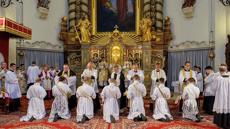 Zeichen der Gemeinschaft: Die anwesenden Priester legen den soeben vom Bischof geweihten Neupriestern ebenfalls die Hände auf.<br>Bild: FSSP Das Photo zeigt die vor dem Hochaltar knienden Weihekandidaten, denen nach der eigentlichen Weihe von den anwesenden Priestern die Hände aufgelegt werden.
