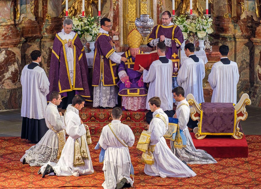 Bild: Website des Seminars Wigratzbad Der Bischof sitzt auf einem Schemel vor dem Altar - die Weihekandidaten knien im Halbkreis davor.