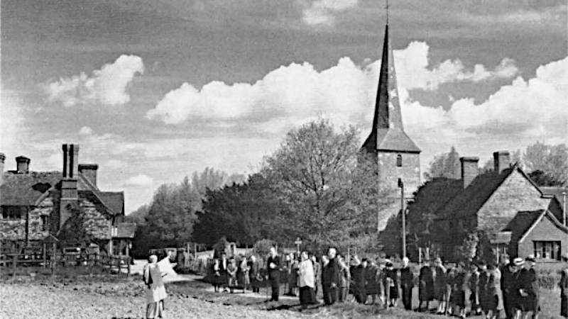 Die Aufnahme aus den 60er Jahren zeigt eine Gruppe von Prozessionsteilnehmern am Dorfrand vor dem Hintergrund der Kirche und einiger Häuser in Kent, England